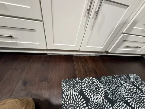 Kitchen floor before repair with an exposed strip along the white cabinets