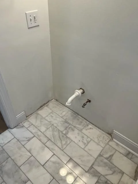 Bathroom vanity space before installation, with wall plumbing exposed above the tile floor