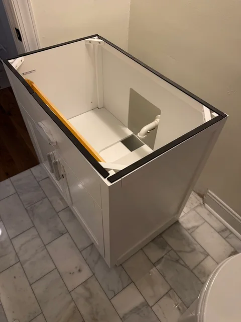 White vanity cabinet positioned around the wall plumbing, with a level across the open top
