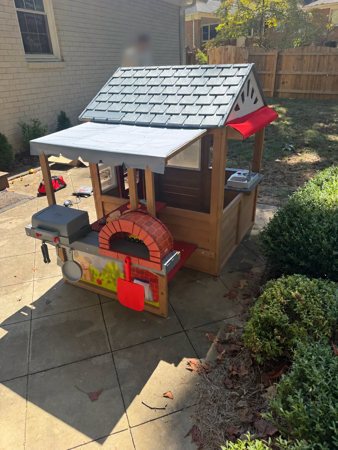 Completed playhouse canopy with a pretend-play grill, pizza oven, and hanging toy utensils