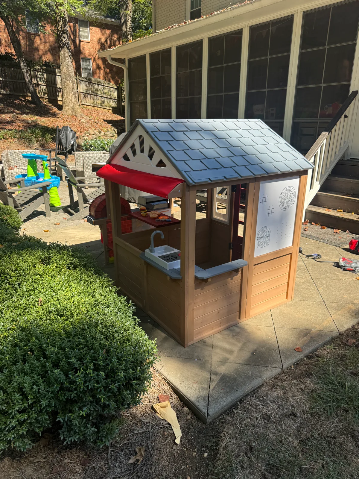 Finished side of the wooden playhouse with a red awning, toy sink, and game panel