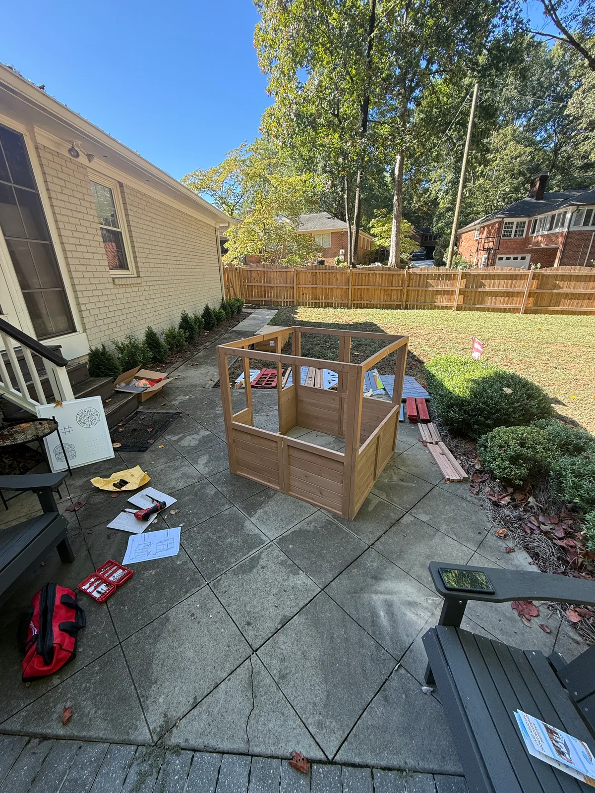 Wooden playhouse wall panels joined upright, with remaining kit parts and tools laid out nearby